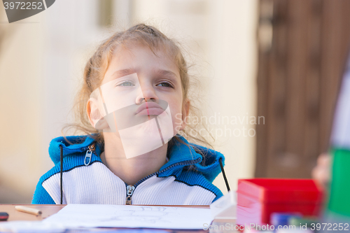 Image of Frustrated girl sitting at a table in the courtyard of the house and looking cocky