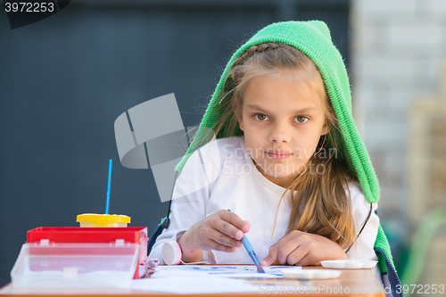 Image of Pleased girl draws paints at the table and looked at the frame