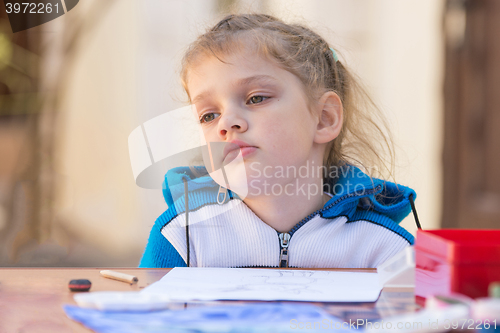 Image of Frustrated girl sitting at a table in the yard and sad looks nowhere
