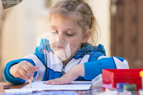 Image of Pretty girls sitting at a table in the courtyard of the house and draws pencil