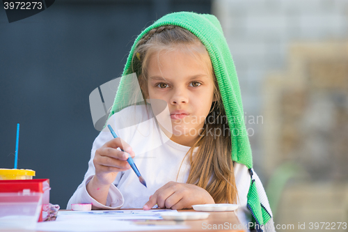 Image of Thoughtful and enthusiastic girl draws a painting at the table and looked at the frame