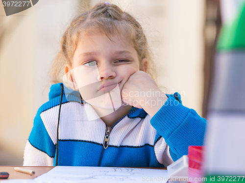 Image of Sad girl thought doing drawing at a table in the yard