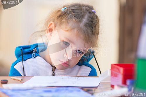 Image of The sad girl sits at a table in the courtyard of the house and does not want to draw