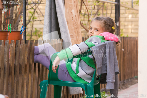 Image of Seven-year girl is resting sitting on a chair in the yard and putting his feet on the wooden fence