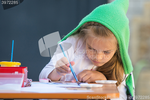 Image of Girl enthusiastically paints watercolors sitting at a table in the yard