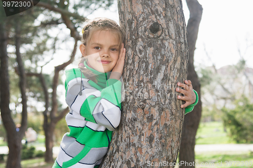 Image of Joyful seven-year old girl sitting on a tree trunk in the early spring