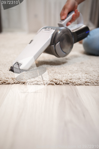 Image of Female hand holding cordless vacuum cleaner and cleaning beige carpet