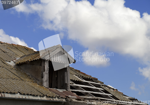 Image of Old tile roof with holes and blue sky with clouds
