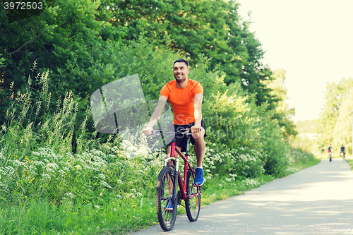 Image of happy young man riding bicycle outdoors