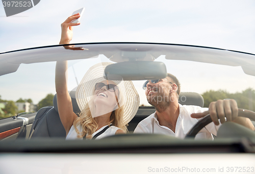 Image of happy couple in car taking selfie with smartphone