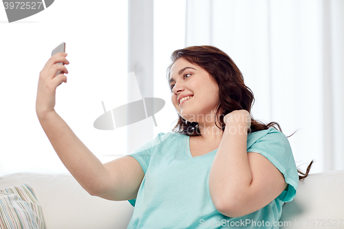 Image of happy plus size woman with smartphone at home