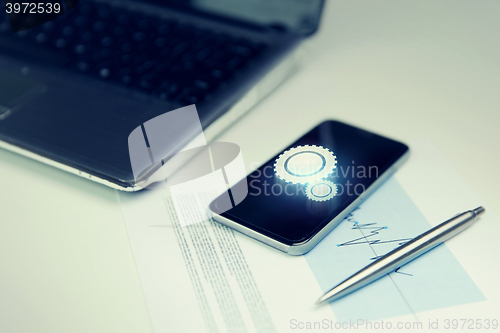 Image of close up of smartphone, laptop and pen on table