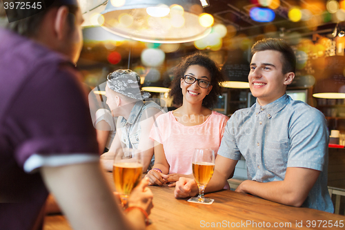 Image of happy friends drinking beer and talking at bar