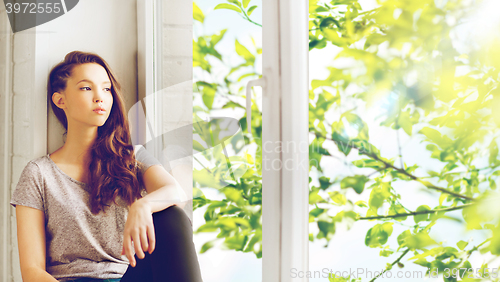 Image of sad pretty teenage girl sitting on windowsill