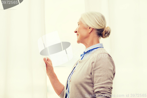 Image of happy senior woman looking through window at home