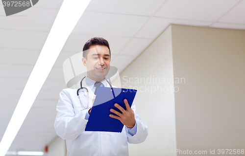 Image of smiling doctor with clipboard at hospital corridor