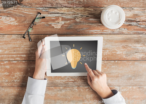 Image of close up of hands with lighting bulb on tablet pc