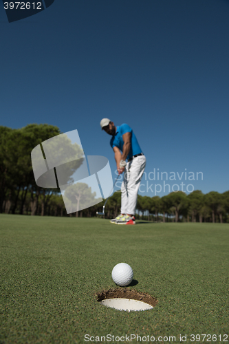 Image of golf player hitting shot, ball on edge of hole