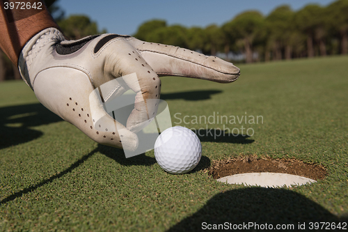 Image of man\'s hand putting golf ball in hole