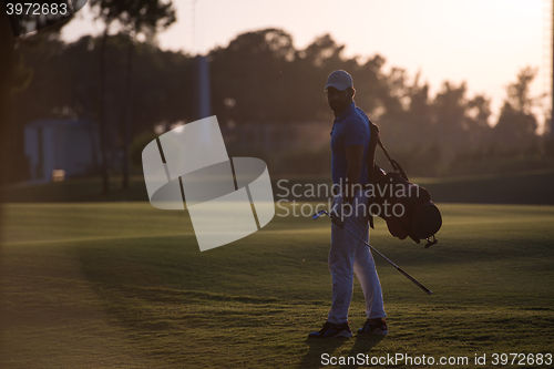 Image of golfer  walking and carrying golf  bag at beautiful sunset