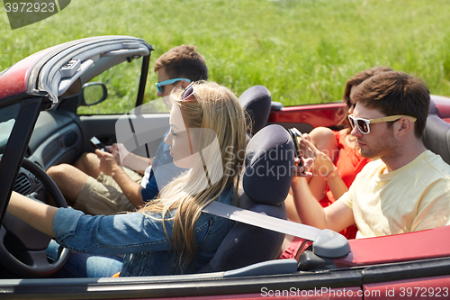 Image of friends with smartphones driving in cabriolet car