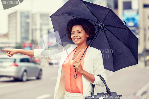 Image of happy african woman with umbrella catching taxi