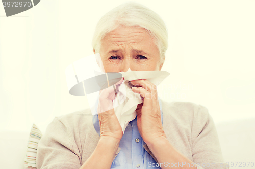 Image of sick senior woman blowing nose to paper napkin