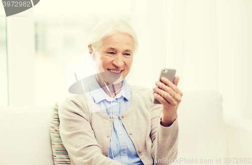 Image of senior woman with smartphone and earphones at home