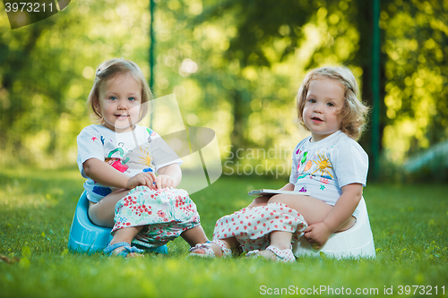 Image of The two little baby girls sitting on pottys against green grass