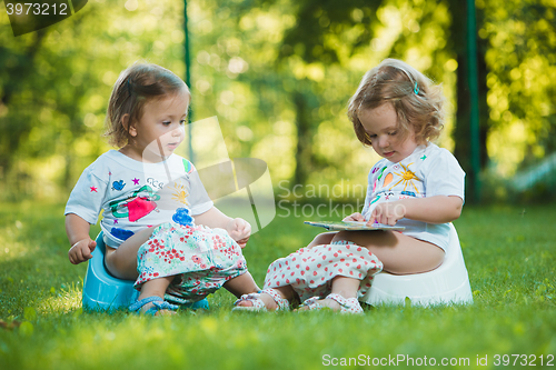 Image of The two little baby girls sitting on pottys against green grass