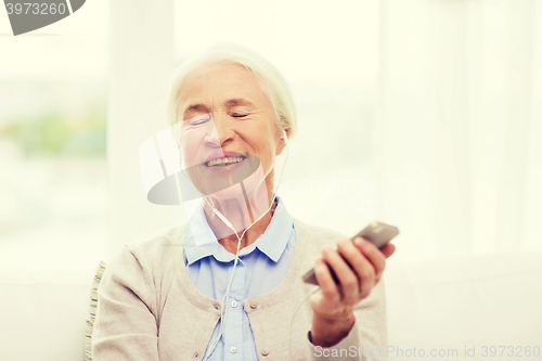 Image of senior woman with smartphone and earphones at home