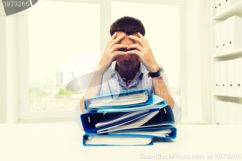 Image of sad businessman with stack of folders at office