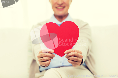 Image of close up of senior woman with red heart at home