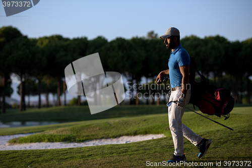 Image of golfer  walking and carrying golf  bag at beautiful sunset