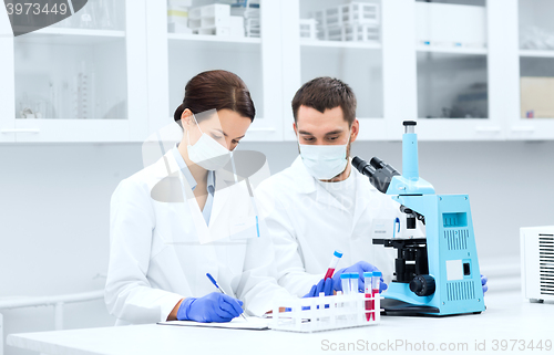 Image of scientists with clipboard and microscope in lab