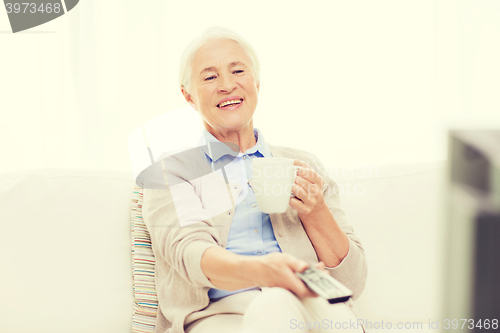 Image of senior woman watching tv and drinking tea at home