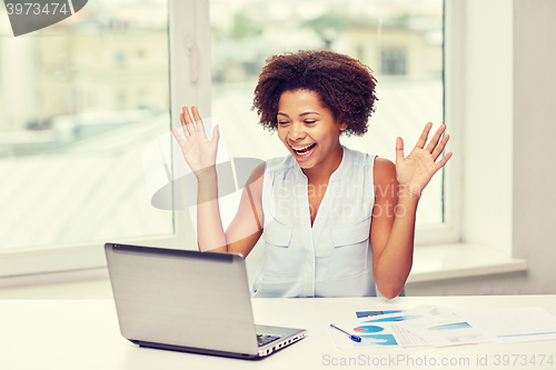 Image of happy african woman with laptop at office