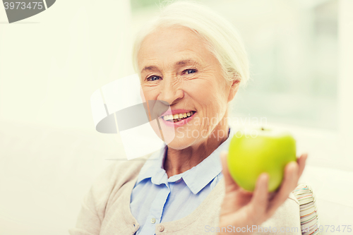 Image of happy senior woman with green apple at home