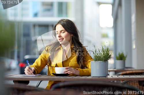 Image of happy woman with notebook drinking cocoa at cafe