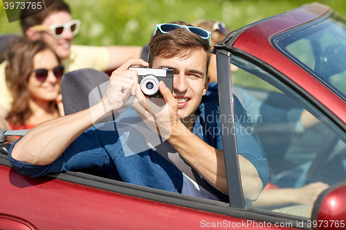 Image of happy friends with camera driving in cabriolet car