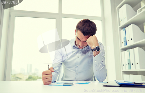Image of stressed businessman with papers in office