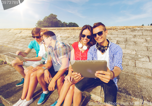 Image of group of smiling friends with tablet pc outdoors