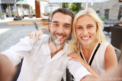 Image of happy couple taking selfie at restaurant terrace