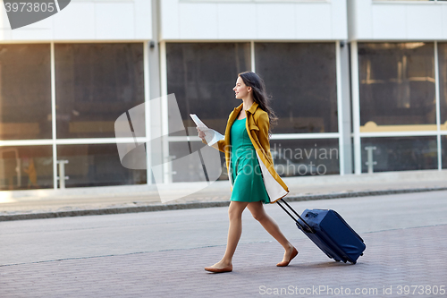 Image of happy young woman with travel bag and map in city