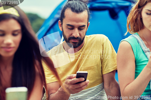 Image of friends with smartphone and tent at camping