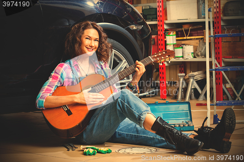 Image of woman mechanic in overalls sitting near the wheels of the car an