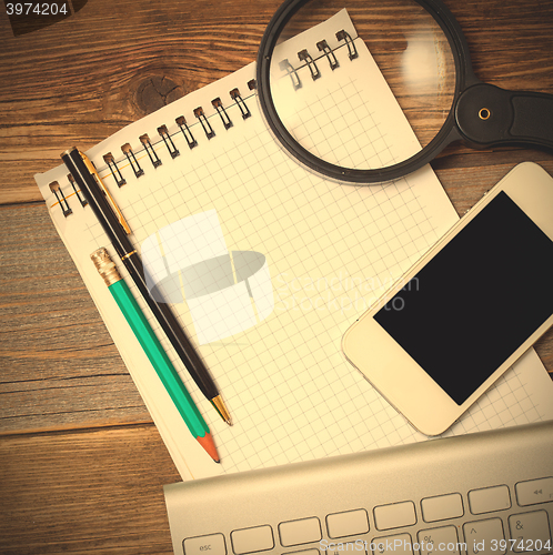 Image of smartphone, computer keyboard, notebook, pen and magnifying glas