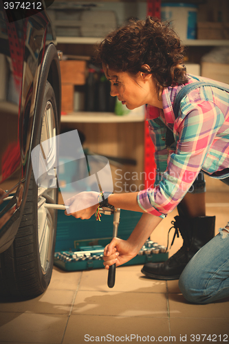 Image of woman mechanic in overalls tighten the fixing bolts on the wheel