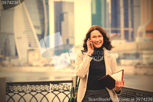 Image of beautiful smiling middle-aged brunette with notebook talking on 