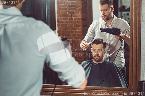 Image of Young handsome barber making haircut of attractive man in barbershop